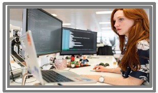 A woman looking at two computer screens.