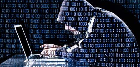 Digital letters and numbers on top of a hooded figure behind a computer. 