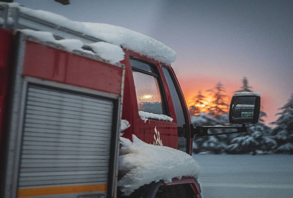A truck with snow on it and a sunset and snowcapped trees in the background.